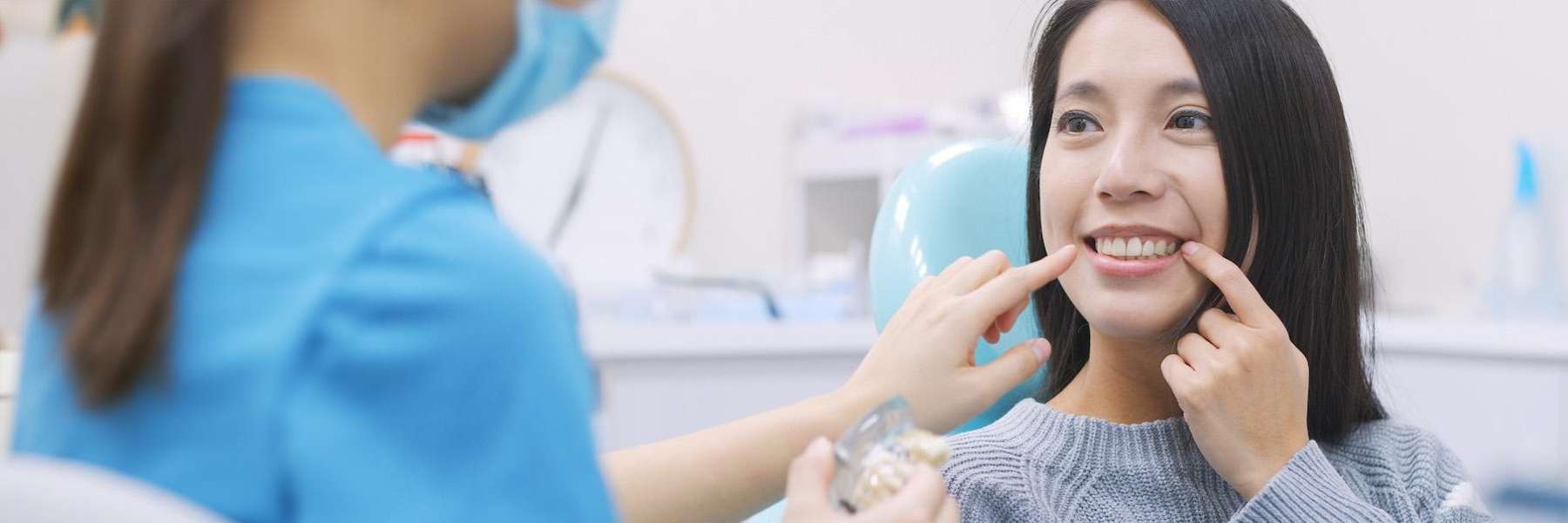 woman sitting in a dental chair pointing at her teeth